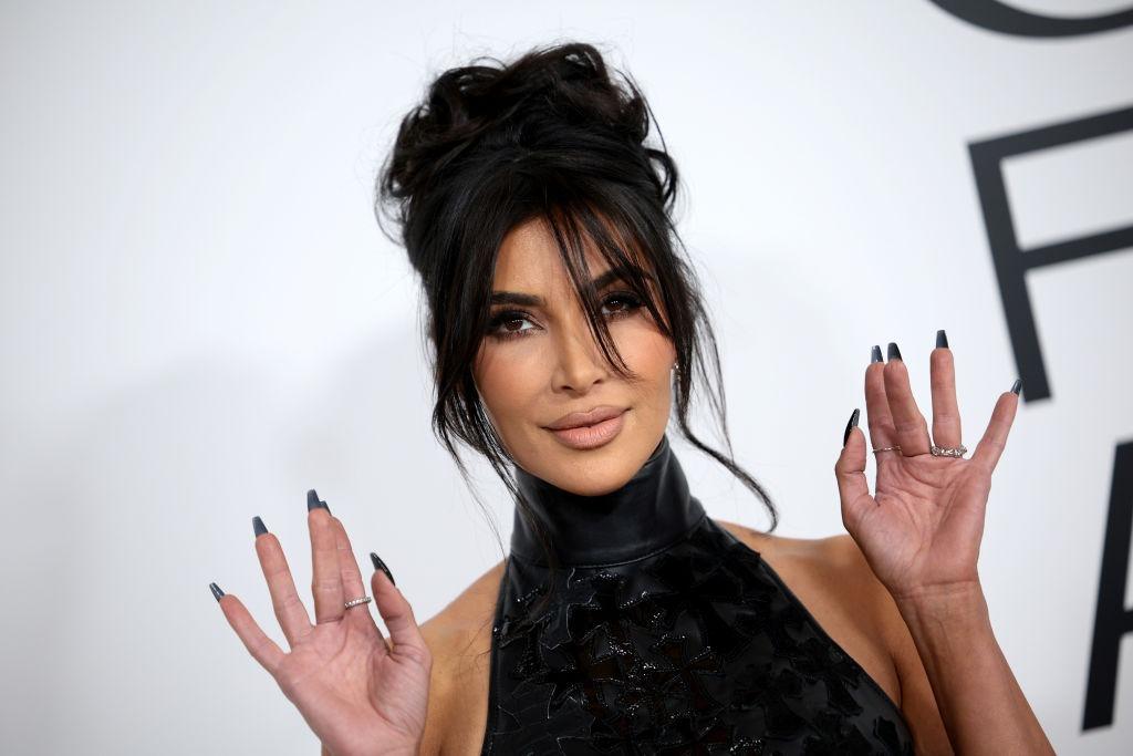 Kim Kardashian îmbrăcată cu un top negru cu guler, ținând mâinile ridicate
