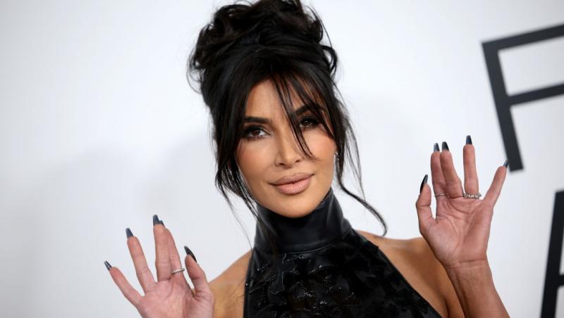 Kim Kardashian îmbrăcată cu un top negru cu guler, ținând mâinile ridicate