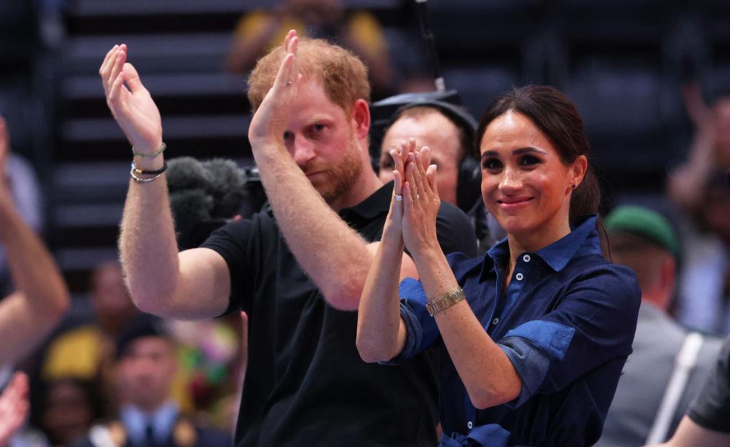 Meghan Markle alături de soțul ei, ambii îmbrăcați casual, aplaudând