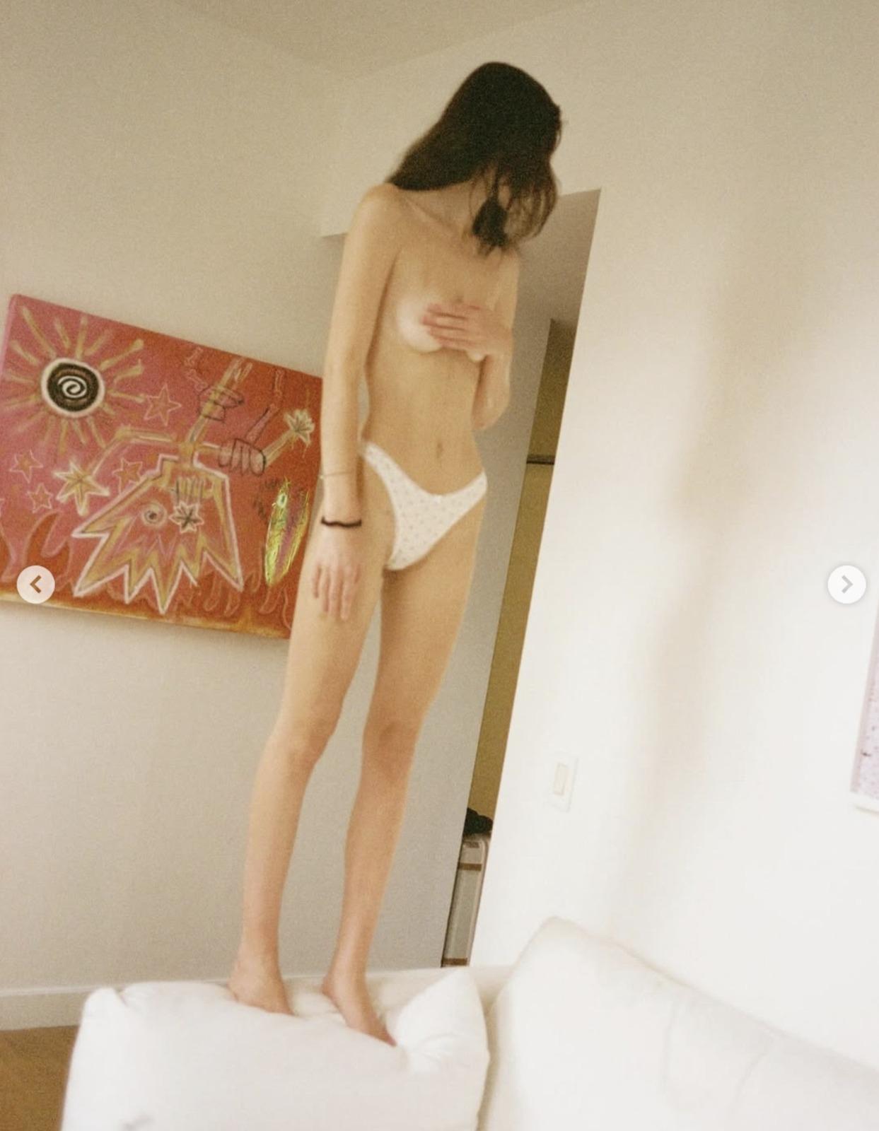 Meadow Walker topless, purtând doar lenjerie albă, stând în picioare pe o canapea