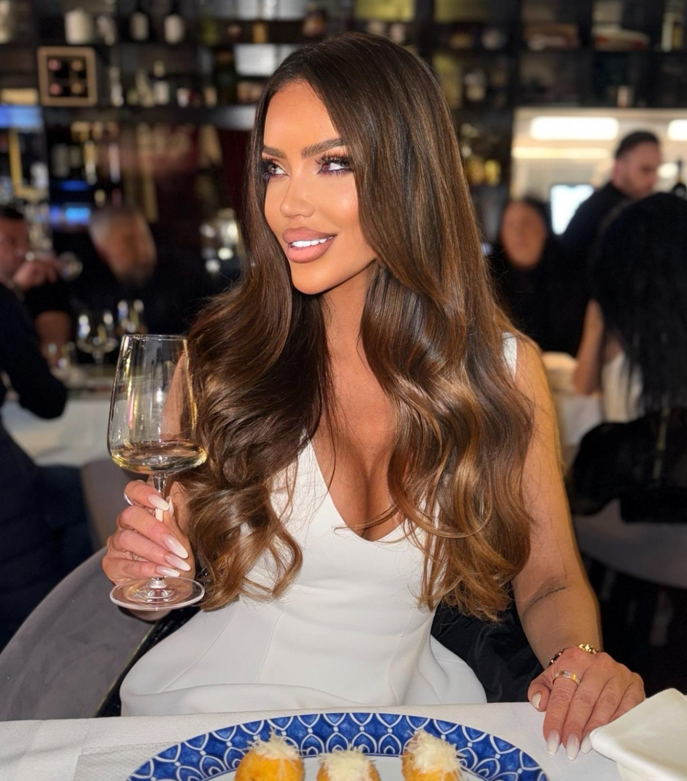 Bianca Dragușanu îmbrăcată cu o rochie albă, ținând un pahar de vin în mână