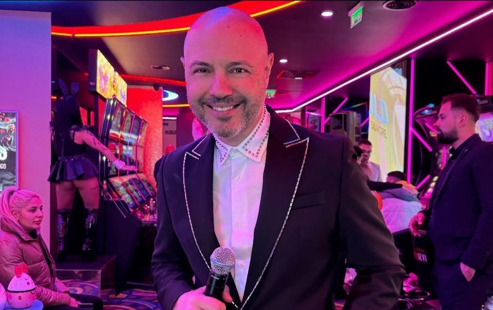 Mihai Mitoșeru îmbrăcat cu un costum negru, ținând un microfon în mână