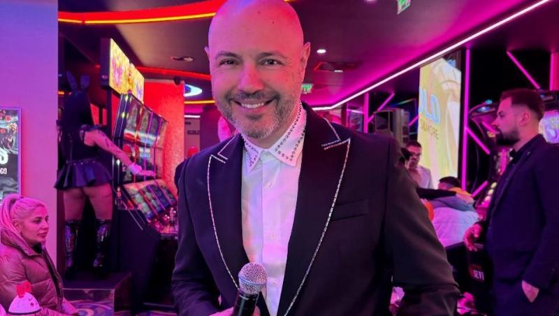 Mihai Mitoșeru îmbrăcat cu un costum negru, ținând un microfon în mână