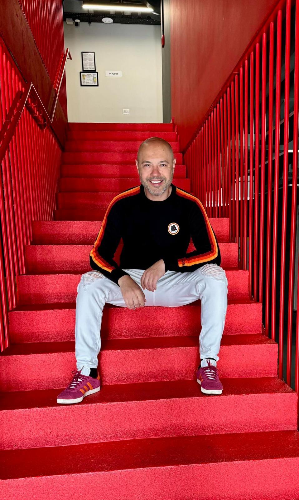 Mihai Mitoșeru îmbrăcat casual, stând pe niște scări de culoare roșie