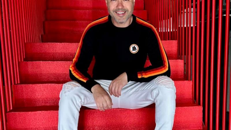 Mihai Mitoșeru îmbrăcat casual, stând pe niște scări de culoare roșie