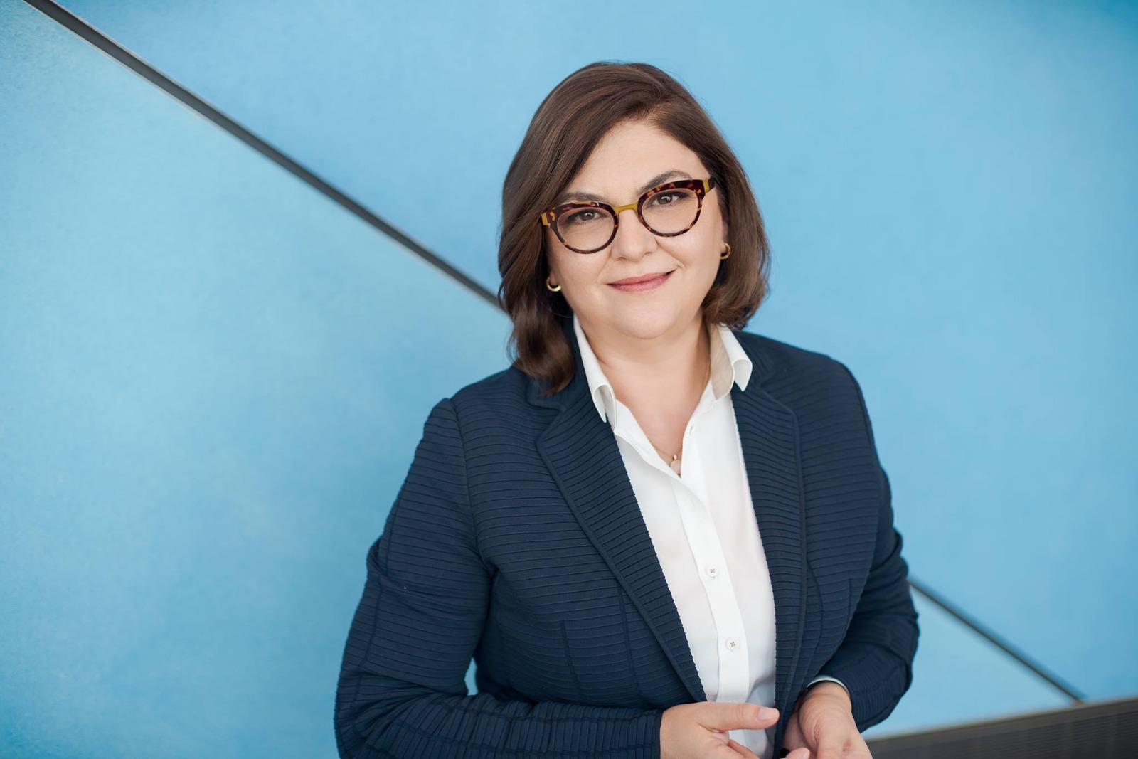 Adina Vălean îmbrăcată cu un sacou bleumarin, peste o cămașă albă