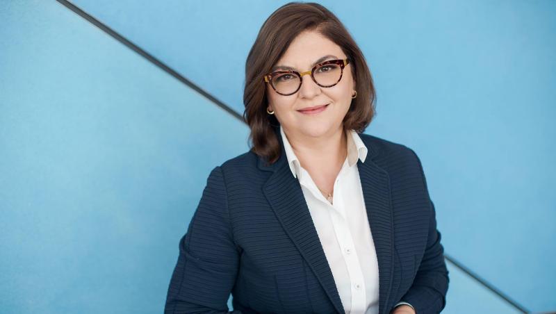 Adina Vălean îmbrăcată cu un sacou bleumarin, peste o cămașă albă