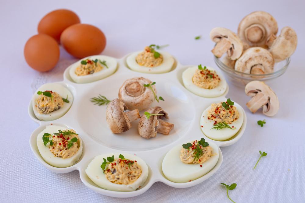 Ouăle umplute cu ciuperci pe un platou alb, cu ouă crude în fundal