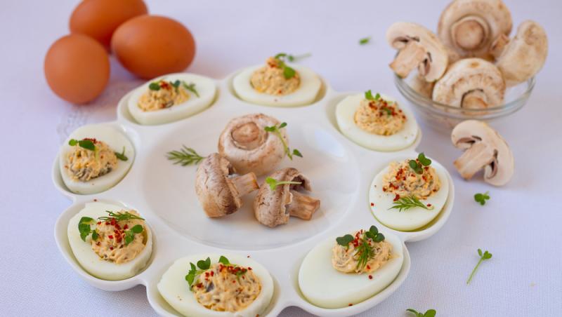 Ouăle umplute cu ciuperci pe un platou alb, cu ouă crude în fundal