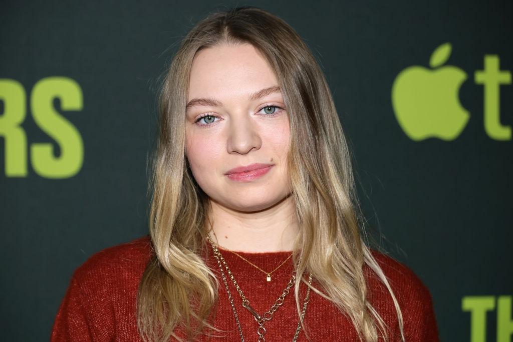 Mia Threapleton îmbrăcată cu o bluză roșie, accesorizată cu mai multe lănțișoare aurii