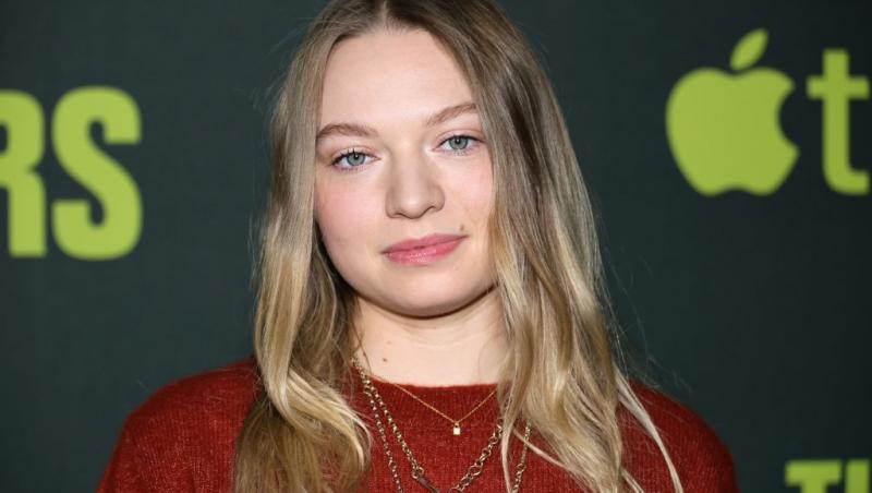 Mia Threapleton îmbrăcată cu o bluză roșie, accesorizată cu mai multe lănțișoare aurii