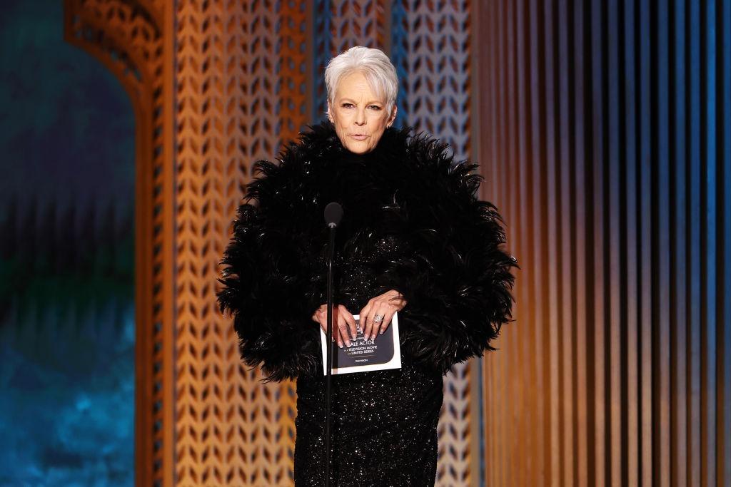 Jamie Lee îmbrăcată cu o rochie neagră pufoasă, vorbind la microfon pe scenă