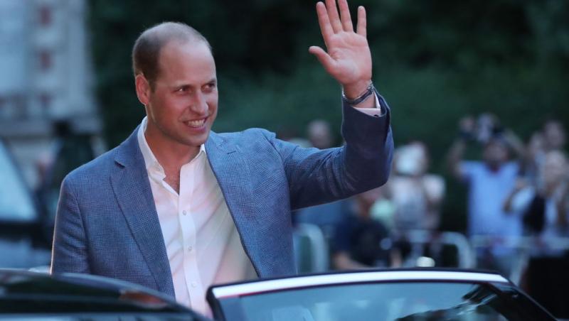Prințul William îmbrăcat într-un costum bleumarin, salutând lumea