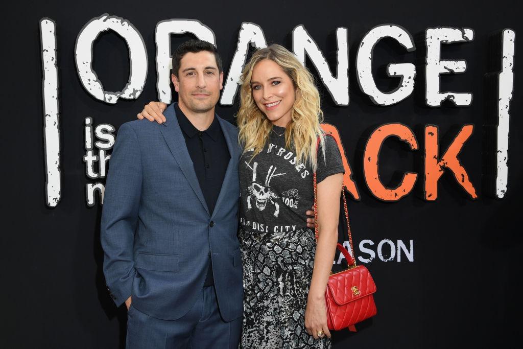 Jason Biggs îmbrăcat cu un costum bleumarin, peste o cămașă neagră, alături de soția lui