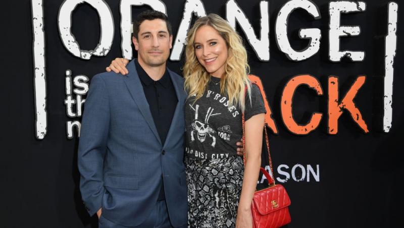 Jason Biggs îmbrăcat cu un costum bleumarin, peste o cămașă neagră, alături de soția lui