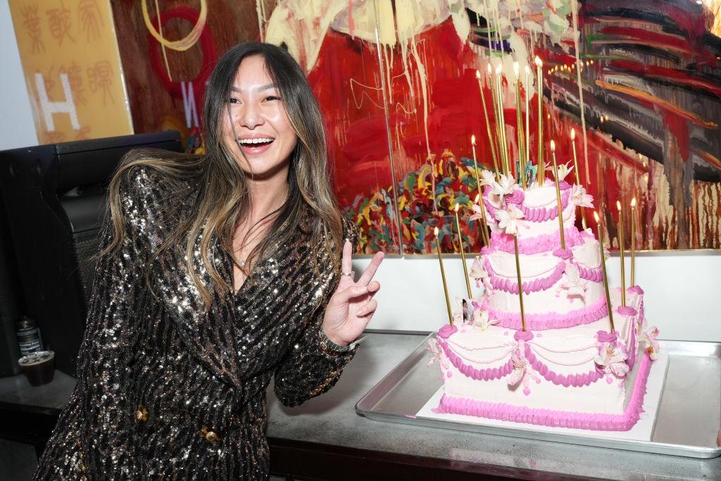 Lucy Guo îmbrăcată într-o ținută strălucitoare, pozând lângă un tort roz