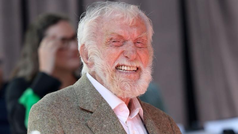 Dick Van Dyke îmbrăcat într-un costum gri, zâmbind fericit