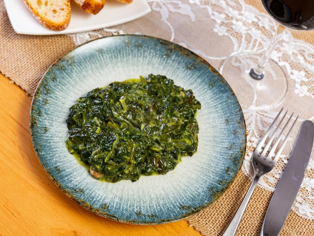 mâncare se spanac într-o farfurie bleu, cu furculiță și cuțit alături