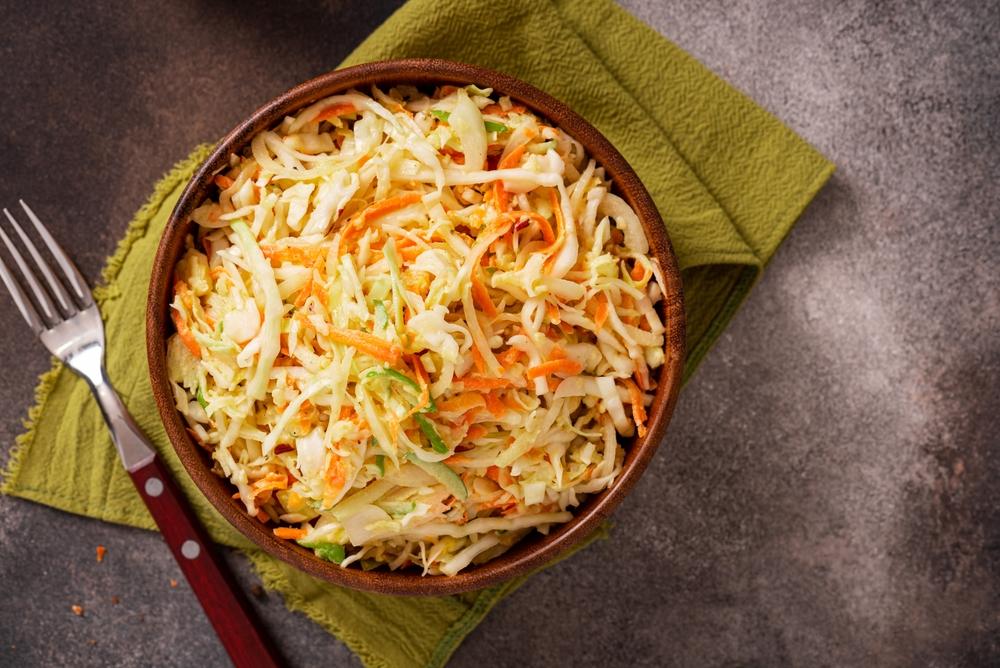 Salata de varză cu morcovi într-un bol maro, pe un ștergar verde