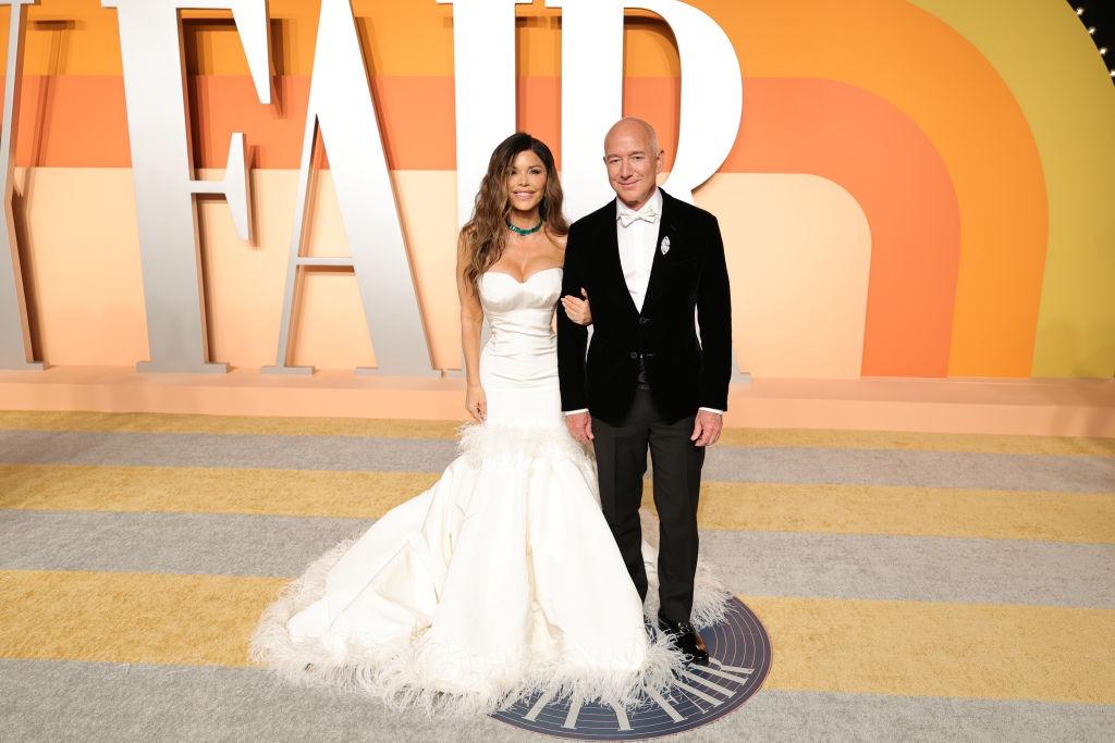Jeff Bezos îmbrăcat în negru, alături de Lauren Sanchez, îmbrăcată într-o rochie albă