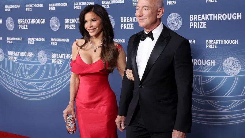 Jeff Bezos îmbrăcat într-un costum negru, alături de Lauren Sanchez, îmbrăcată într-o rochie roșie