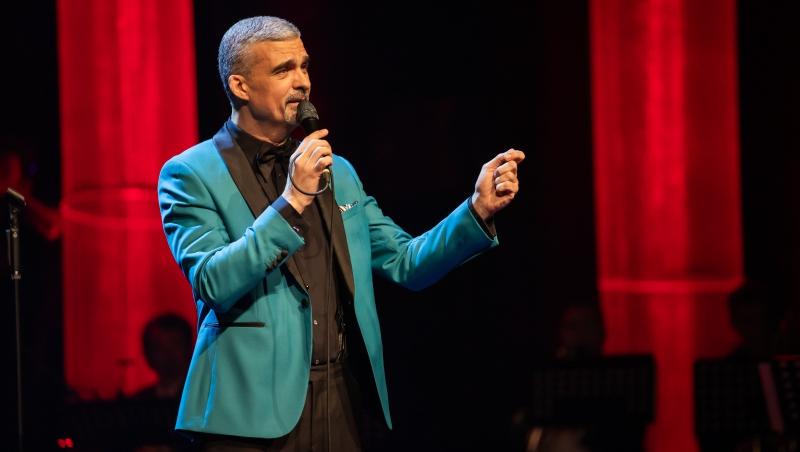 Aurelian Temișan îmbrăcat cu un costum bleu cu revere negre, cântând la microfon