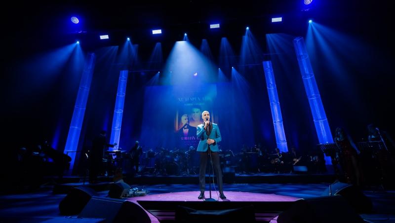 Aurelian Temișan îmbrăcat cu un costum bleu cu revere negre, cântând la microfon