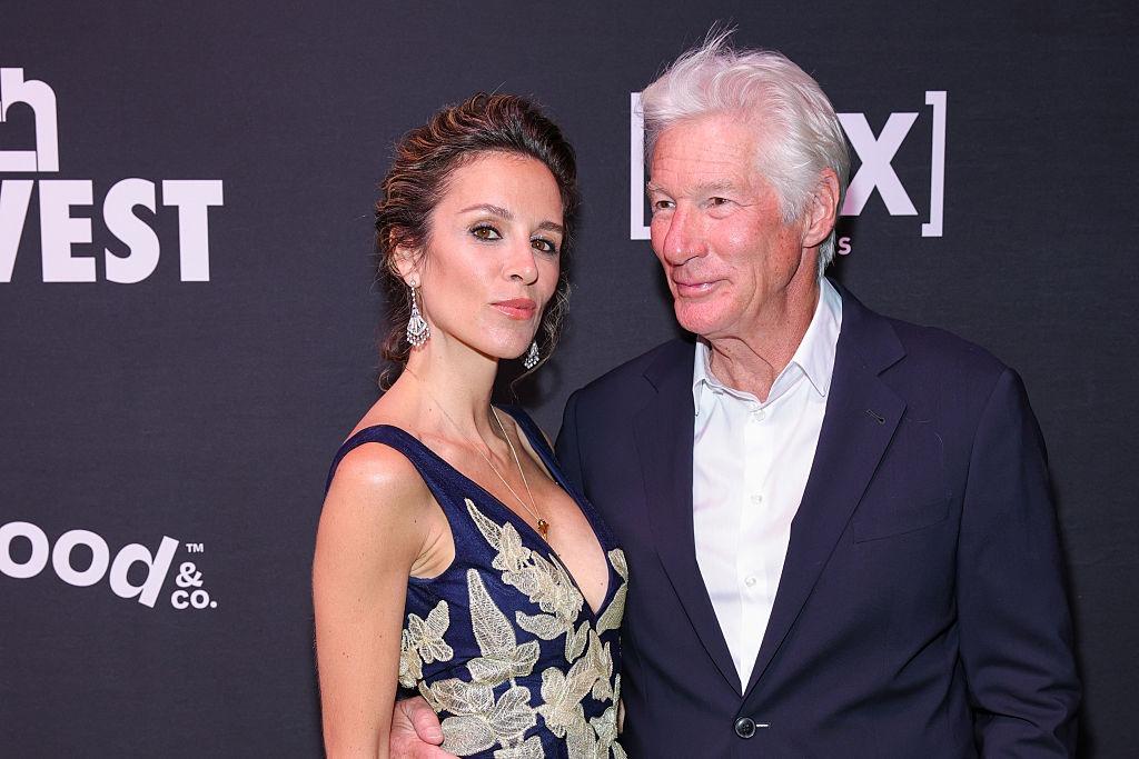 Richard Gere îmbrăcat cu un costum bleumarin peste o cămașă albă, alături de soția lui, îmbrăcată cu o rochie elegantă