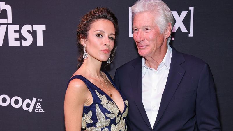 Richard Gere îmbrăcat cu un costum bleumarin peste o cămașă albă, alături de soția lui, îmbrăcată cu o rochie elegantă