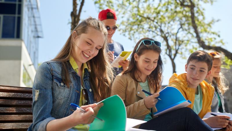 imagine cu un grup de adolescenti care au caiete in maini pe o banca in curte