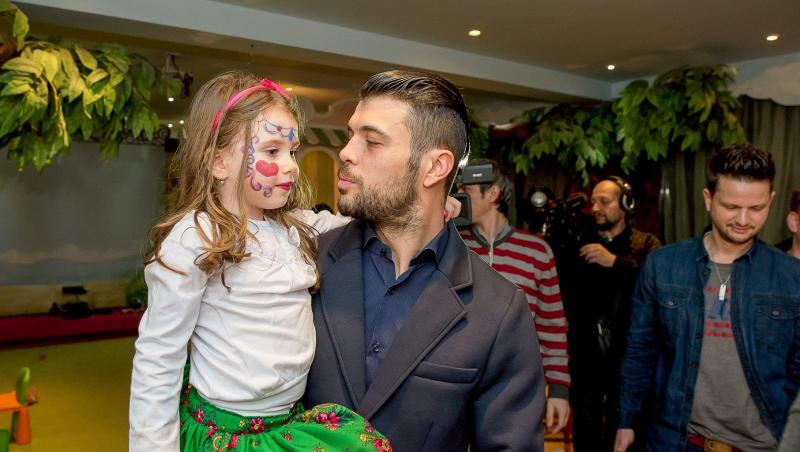 Marius Elisei îmbrăcat cu un costum gri, ținând-o în brațe pe fiica sa