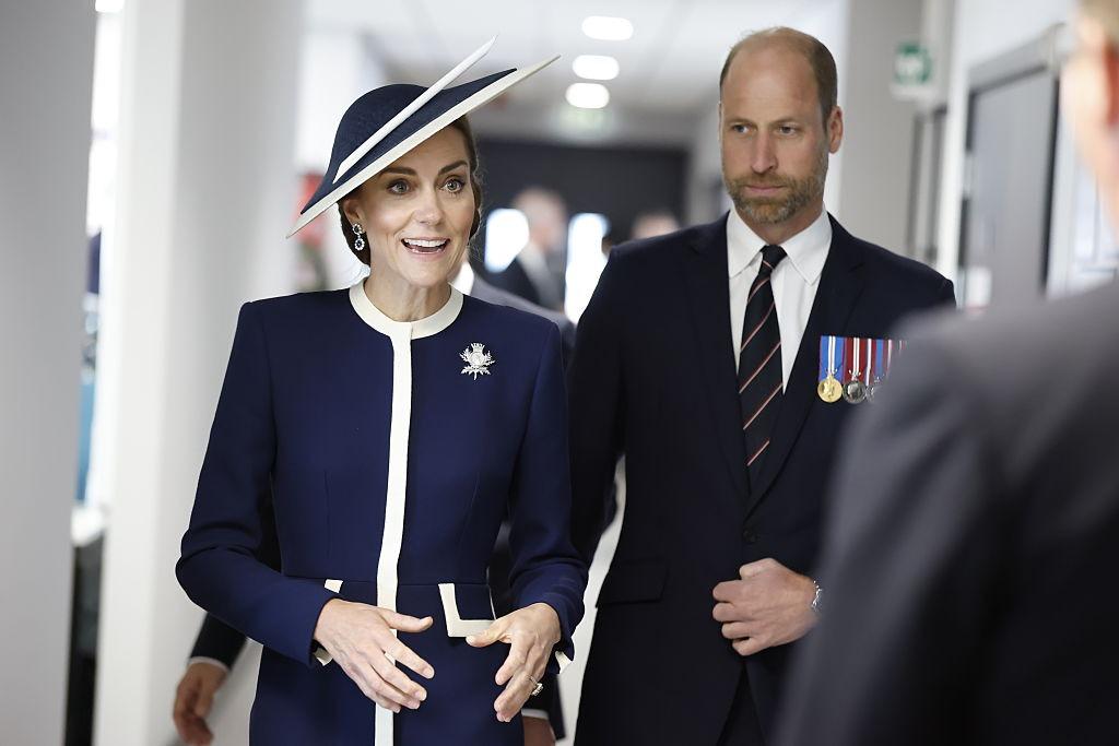 Prințul William îmbrăcat într-un costum negru, alături de Prințesa Kate, îmbrăcată într-o ținută elegantă bleumarin