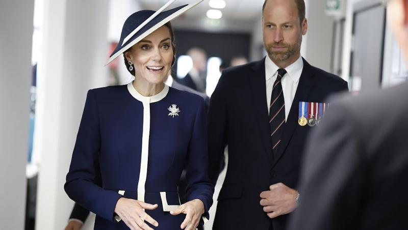 Prințul William îmbrăcat într-un costum negru, alături de Prințesa Kate, îmbrăcată într-o ținută elegantă bleumarin