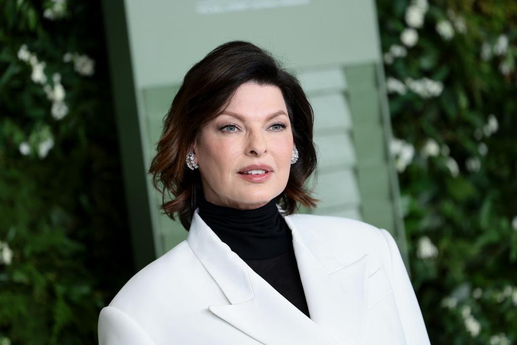 Linda Evangelista îmbrăcată cu un sacou alb peste o bluză neagră