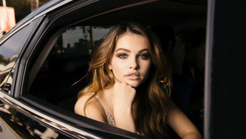 Thylane Blondeau îmbrăcată într-o rochie bej fără mâneci, privind de pe geamul unei mașini