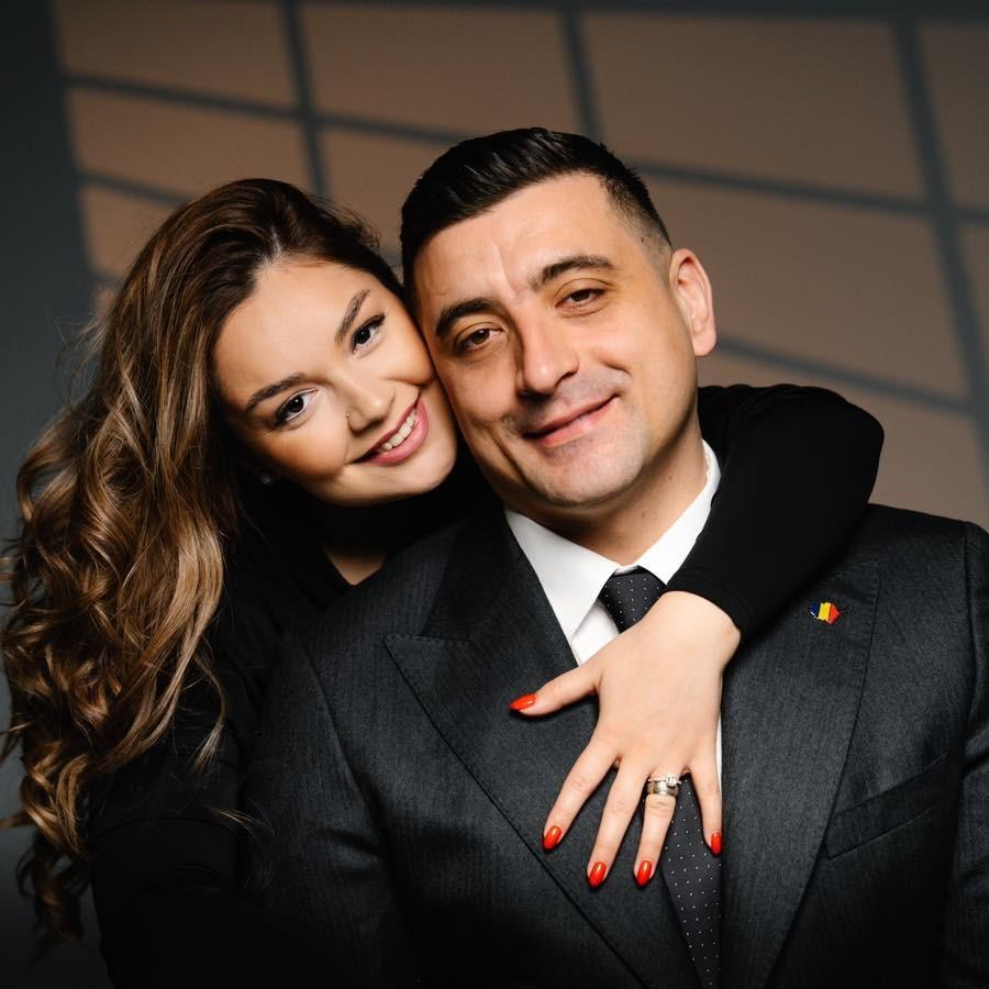 George Simion îmbrăcat într-un costum negru, îmbrățișat de la spate de soția lui