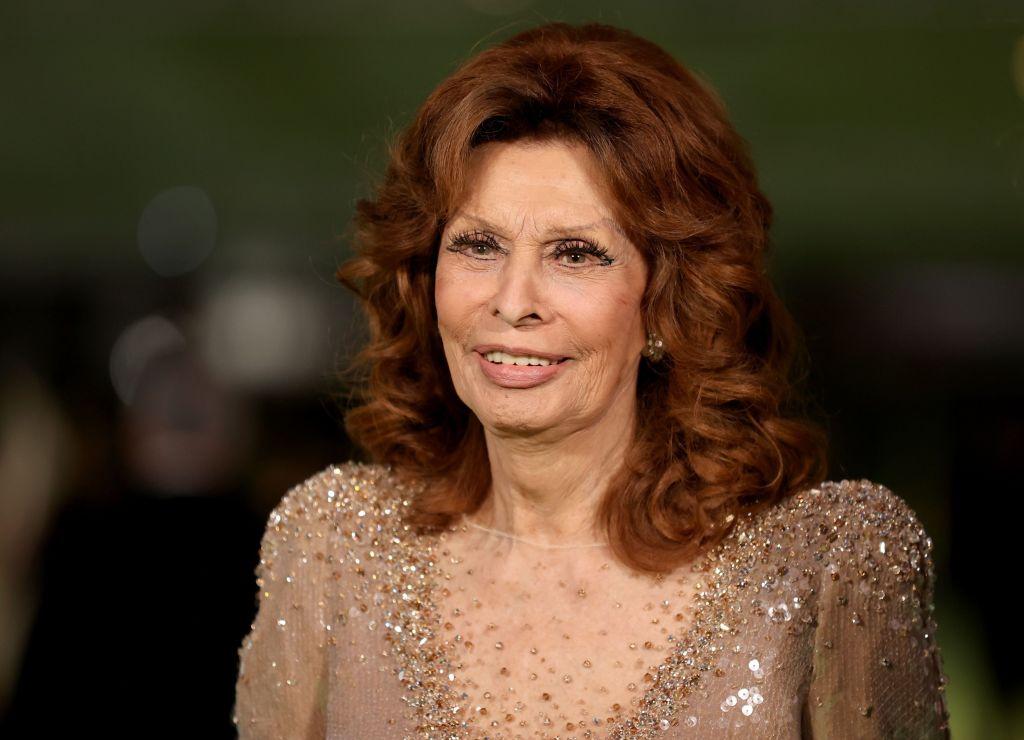 Sophia Loren îmbrăcată într-o rochie de gală bej, cu părul roșcat coafat în bucle voluminoase