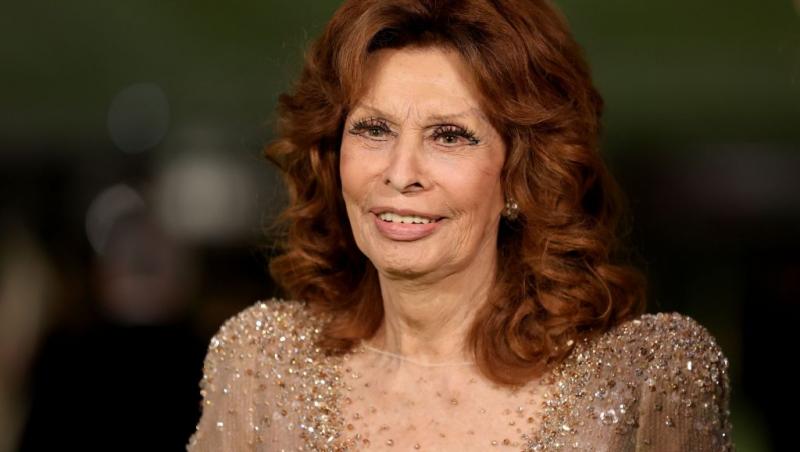 Sophia Loren îmbrăcată într-o rochie de gală bej, cu părul roșcat coafat în bucle voluminoase