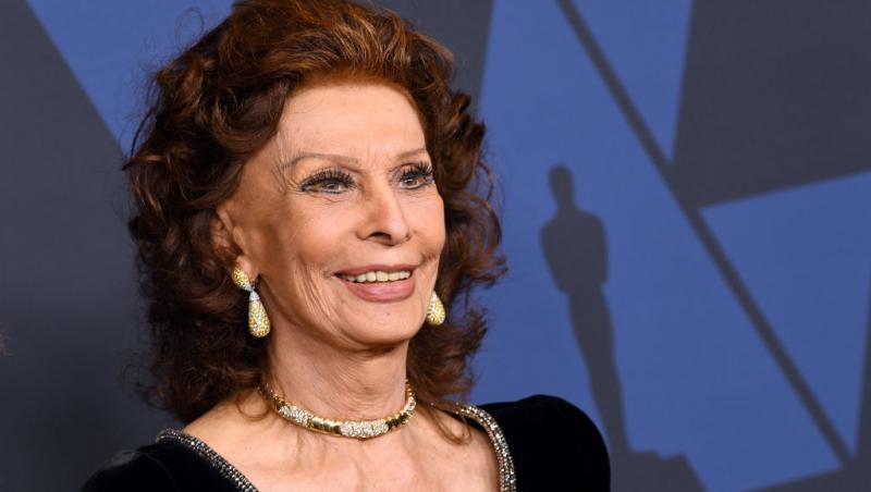 Sophia Loren îmbrăcată într-o rochie neagră de catifea, cu accesorii aurii și părul coafat în bucle
