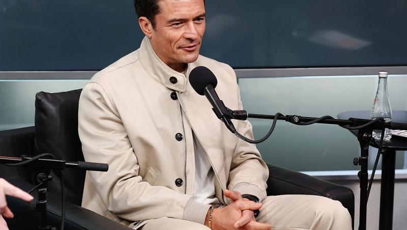 Orlando Bloom îmbrăcat cu o ținută bej, vorbind la microfon