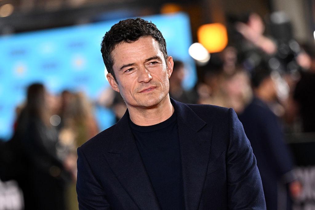 Orlando Bloom îmbrăcat cu un sacou negru, peste o bluză neagră