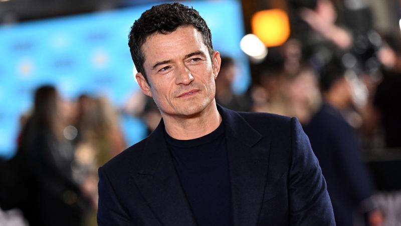 Orlando Bloom îmbrăcat cu un sacou negru, peste o bluză neagră