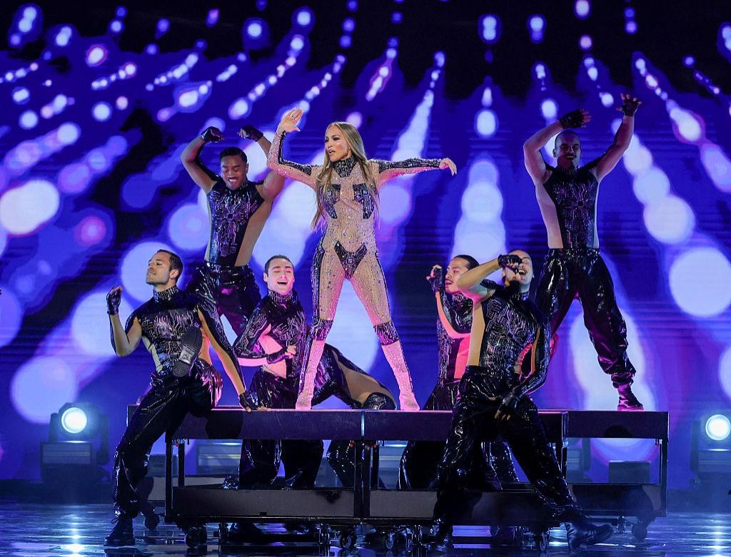 Jennifer Lopez îmbrăcată cu o ținută strălucitoare, dansând pe scenă cu echipa ei