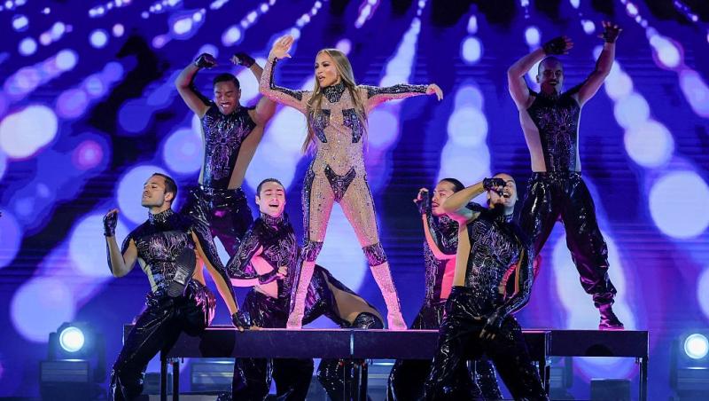 Jennifer Lopez îmbrăcată cu o ținută strălucitoare, dansând pe scenă cu echipa ei