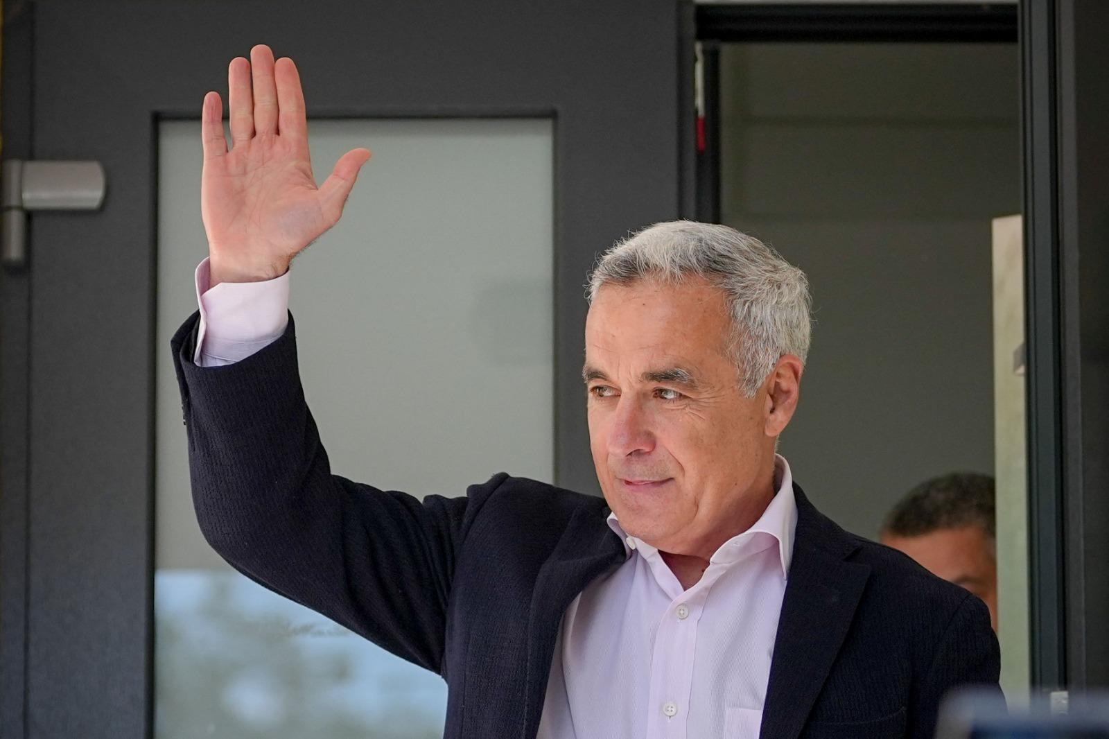 Călin Georgescu îmbrăcat într-un sacou negru, peste o cămașă roz, salutând oamenii