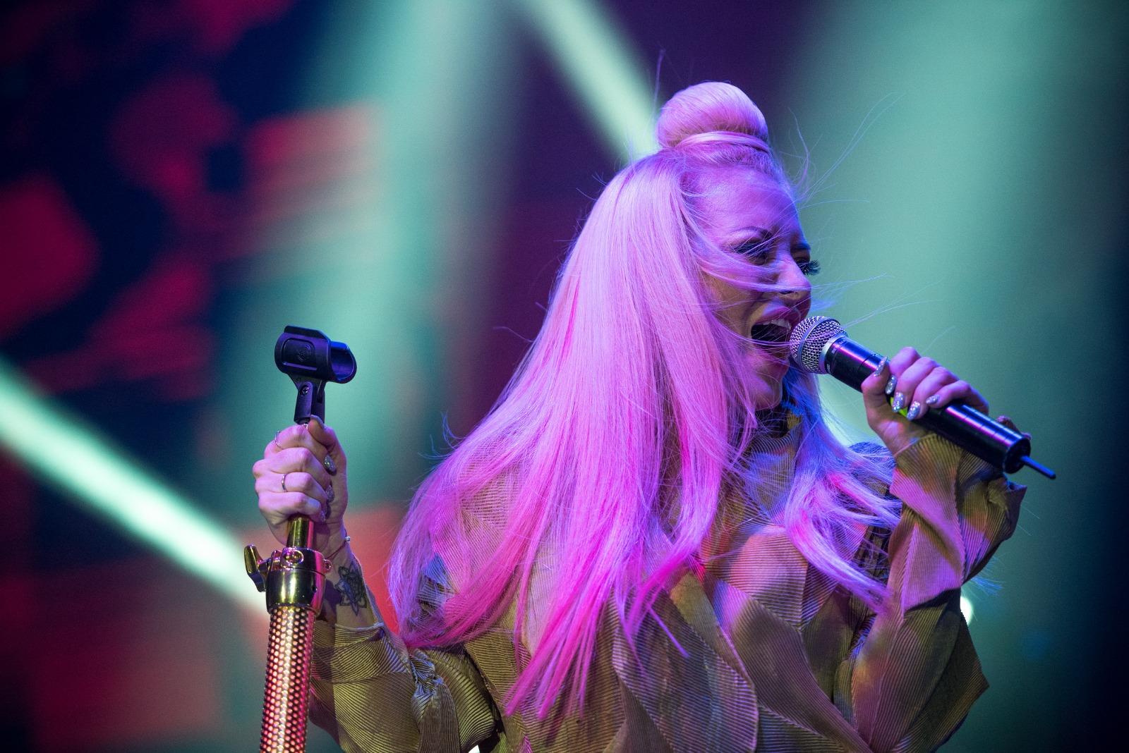 Delia îmbrăcată într-o ținută aurie, cântând la microfon pe scenă