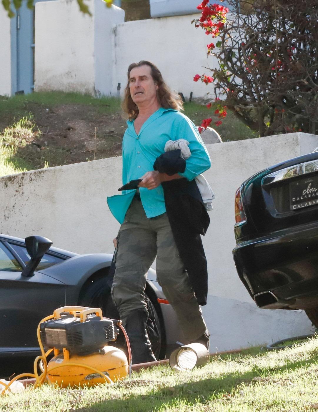 Fabio Lanzoni îmbrăcat cu o cămașă bleu și pantaloni kaki, mergând și vorbind la telefon