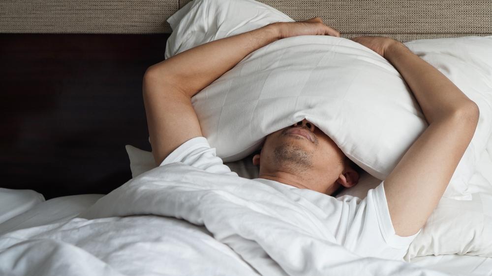 barbat intins in pat isi tine perna pe fata