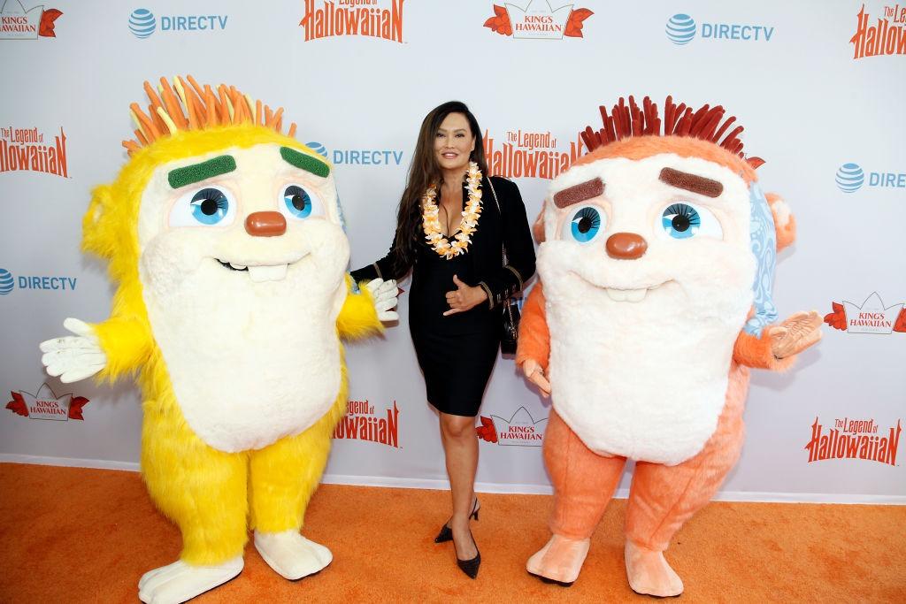 Tia Carrere îmbrăcată într-o rochie neagră mulată, alături de două mascote