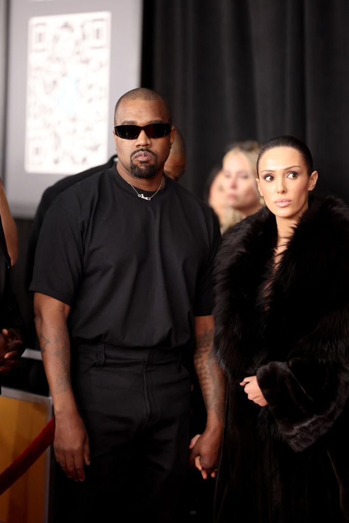 Bianca Censori îmbrăcată cu o haină neagră pufoasă, alături de Kanye West, îmbrăcat în negru
